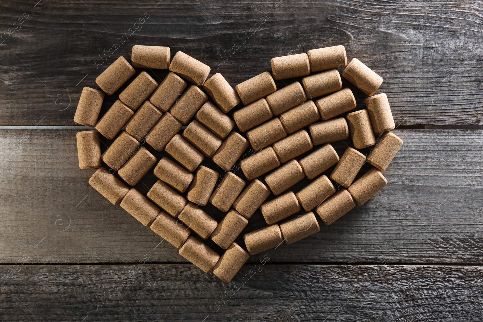 Photo of Heart made of wine bottle corks on wooden table, top view