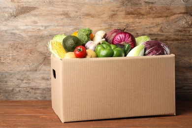 Photo of Fresh vegetables in cardboard box on wooden table