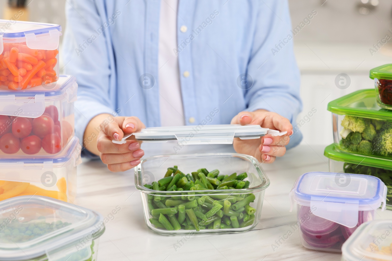 Photo of Woman sealing container with green beans at white marble table in kitchen, closeup. Food storage