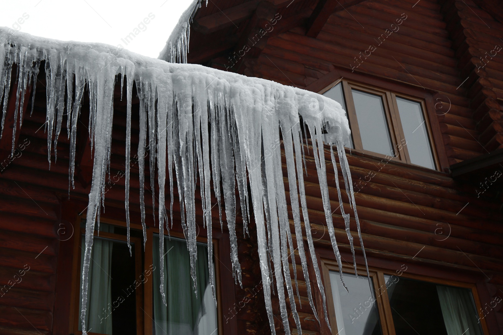 Photo of House with icicles on roof, low angle view. Winter season