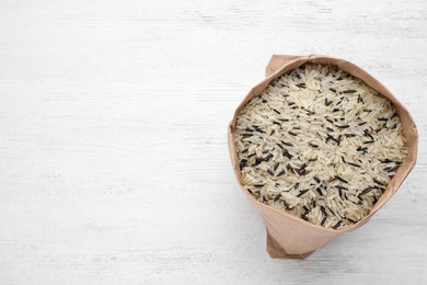 Photo of Mix of brown and polished rice in paper bag on white wooden table, top view