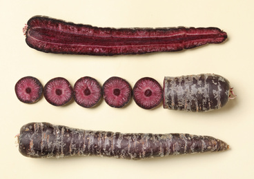 Photo of Whole and cut raw purple carrots on beige background, flat lay