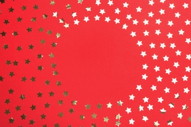 Photo of Frame of confetti stars with space for text on red background, top view. Christmas celebration