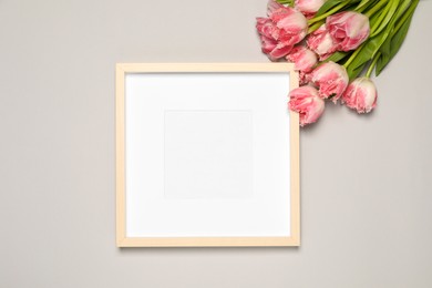 Photo of Empty photo frame and beautiful tulip flowers on light gray background, flat lay. Mockup for design