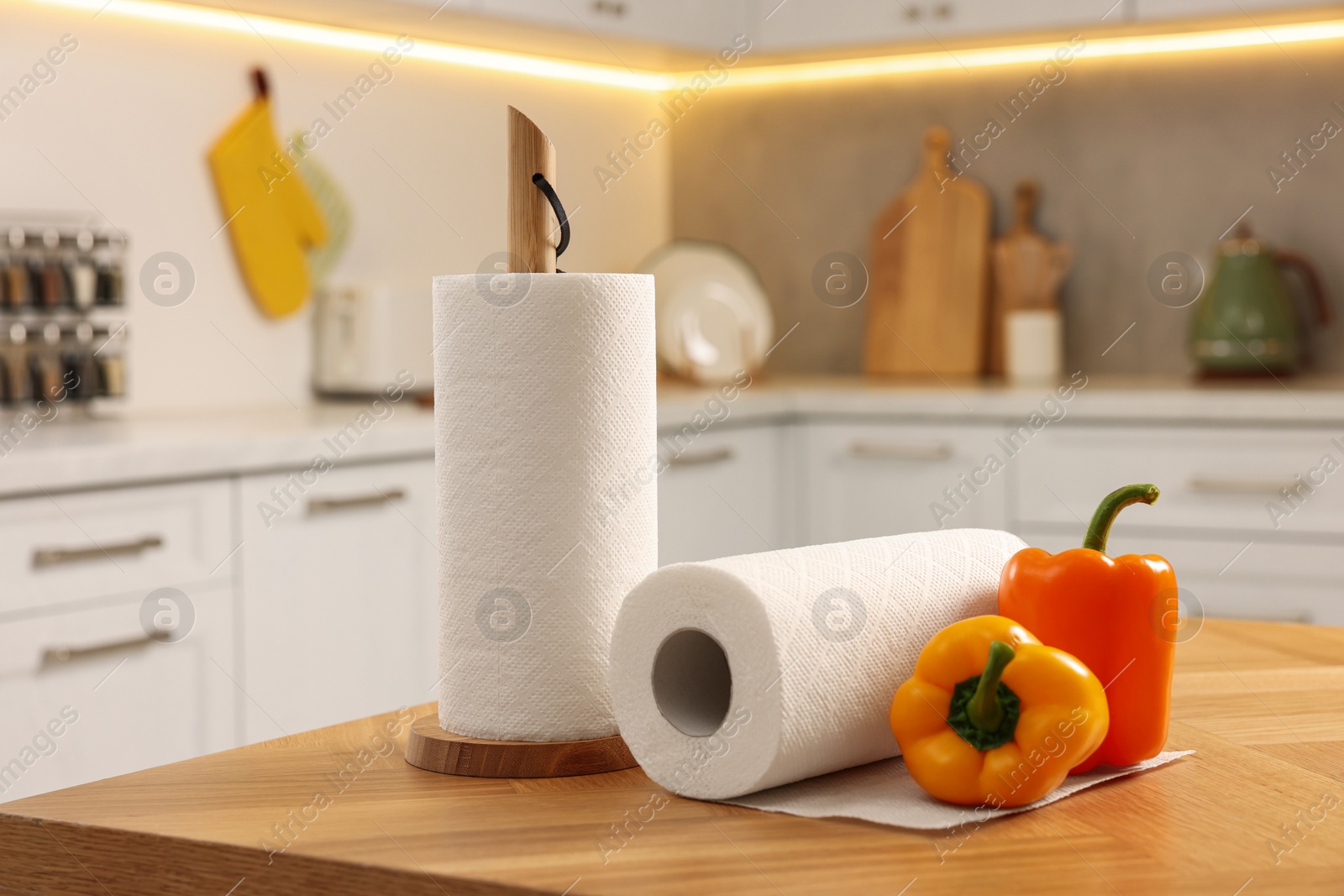 Photo of Rolls of white paper towels and bell peppers on wooden table in kitchen