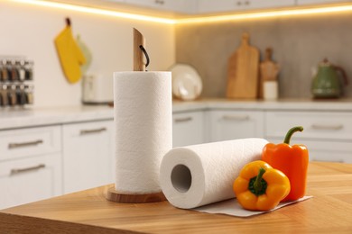 Photo of Rolls of white paper towels and bell peppers on wooden table in kitchen
