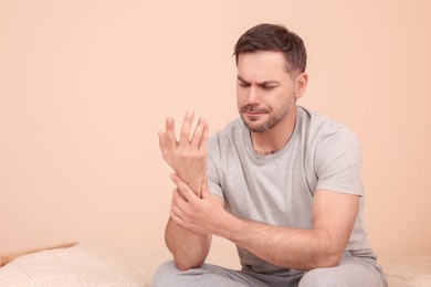 Photo of Man suffering from pain in his hand on bed indoors