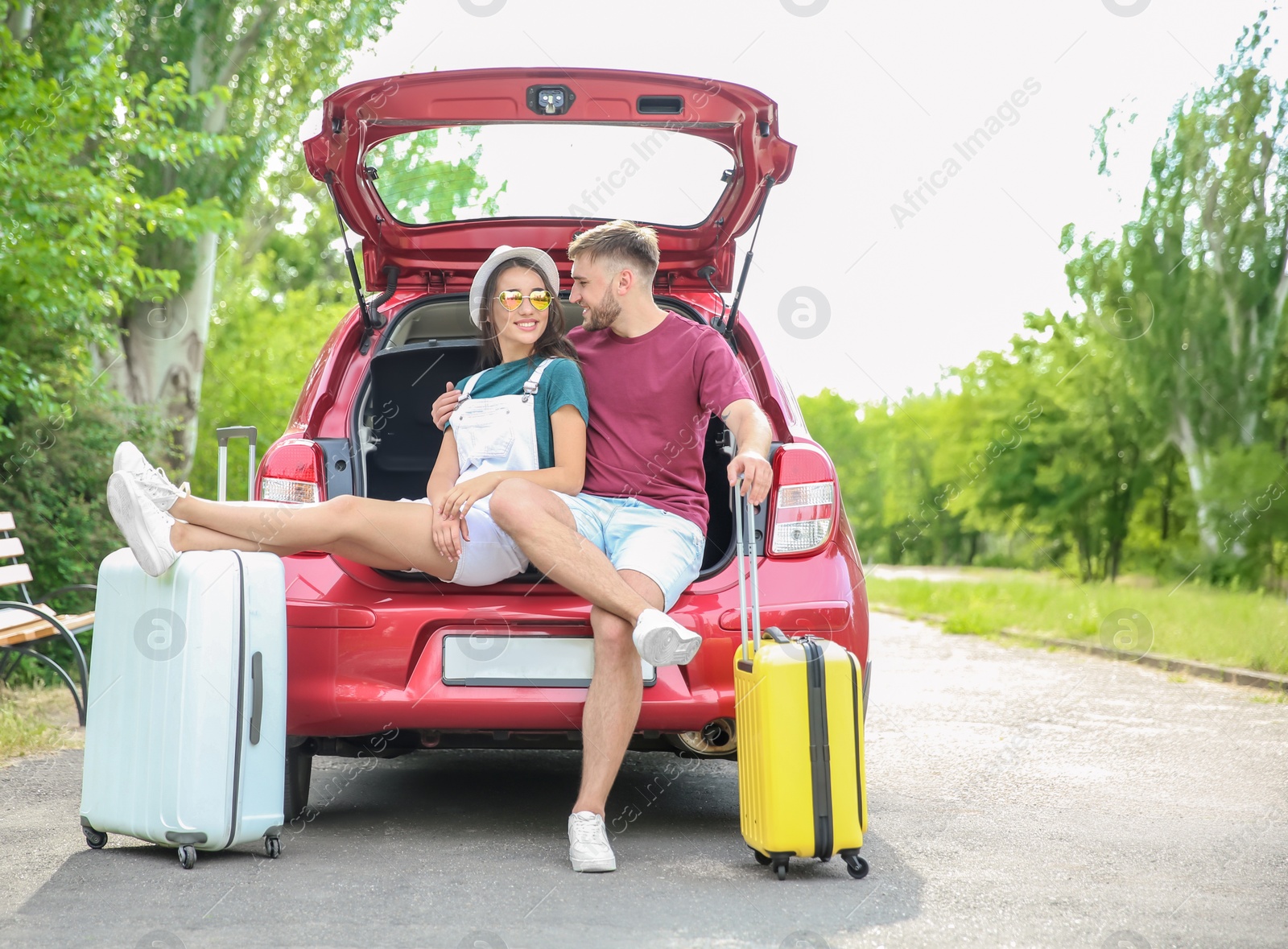 Photo of Beautiful young couple with suitcases packed for summer journey sitting in car trunk