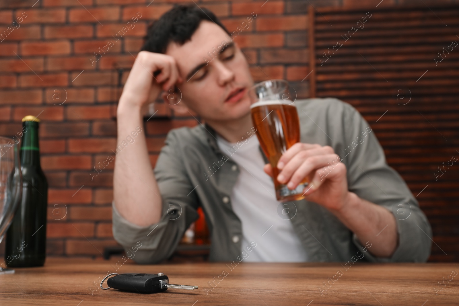 Photo of Man holding glass of alcoholic drink and sitting at table with car keys, selective focus. Don't drink and drive concept