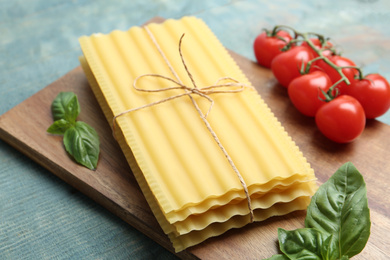 Photo of Uncooked lasagna sheets with basil and cherry tomatoes on blue wooden table, closeup