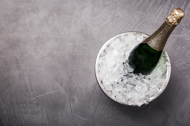 Photo of Champagne in metal bucket with ice on grey table, top view. Space for text