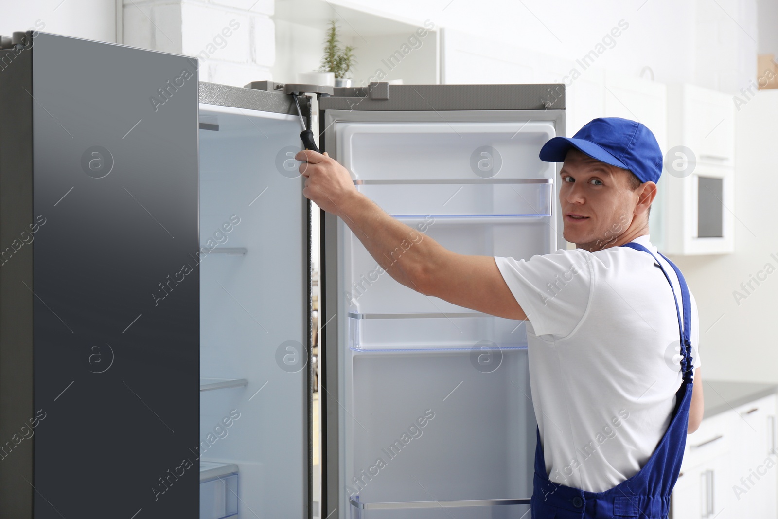 Photo of Male technician with screwdriver repairing refrigerator in kitchen