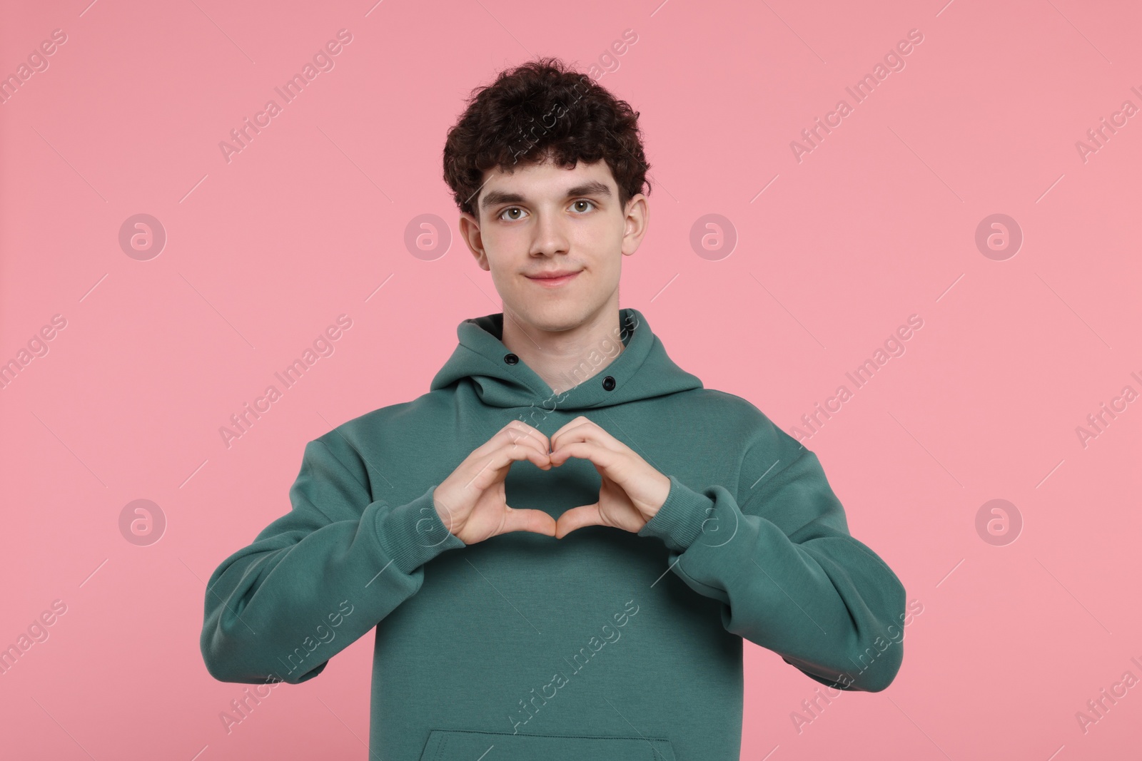 Photo of Happy young man showing heart gesture with hands on pink background