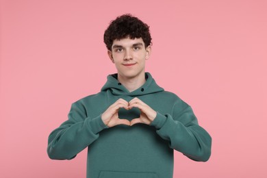 Happy young man showing heart gesture with hands on pink background