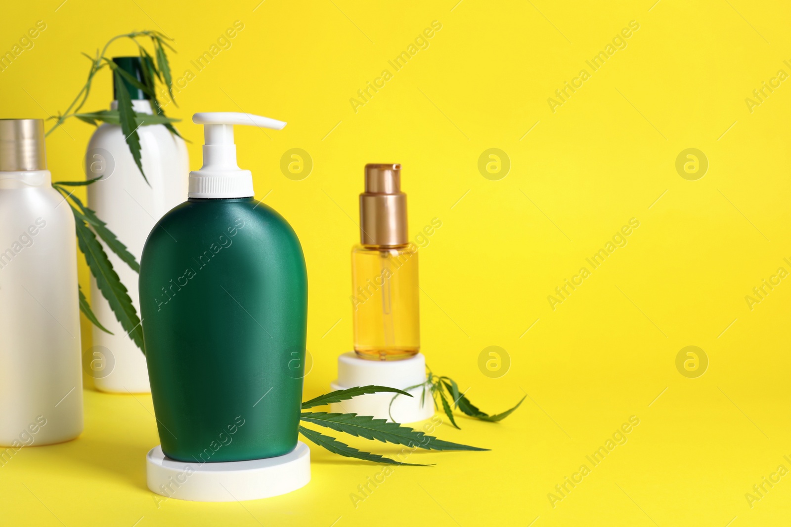 Photo of Bottles of hemp cosmetics and green leaves on yellow background, space for text