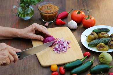 Photo of Woman cutting red onion for salsa sauce at wooden table, closeup