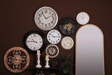 Mirror and collection of clocks on brown wall indoors