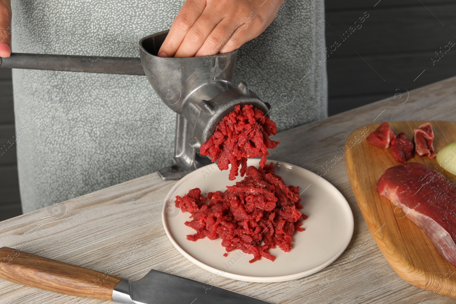 Photo of Woman making beef mince with manual meat grinder at light wooden table, closeup