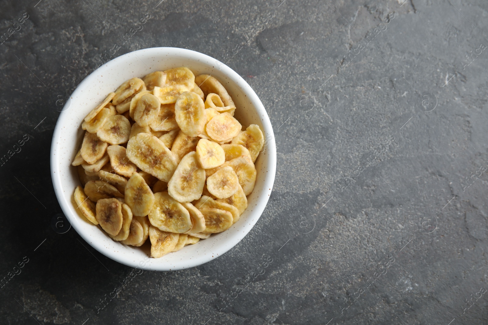 Photo of Bowl with sweet banana slices on grey background, top view with space for text. Dried fruit as healthy snack