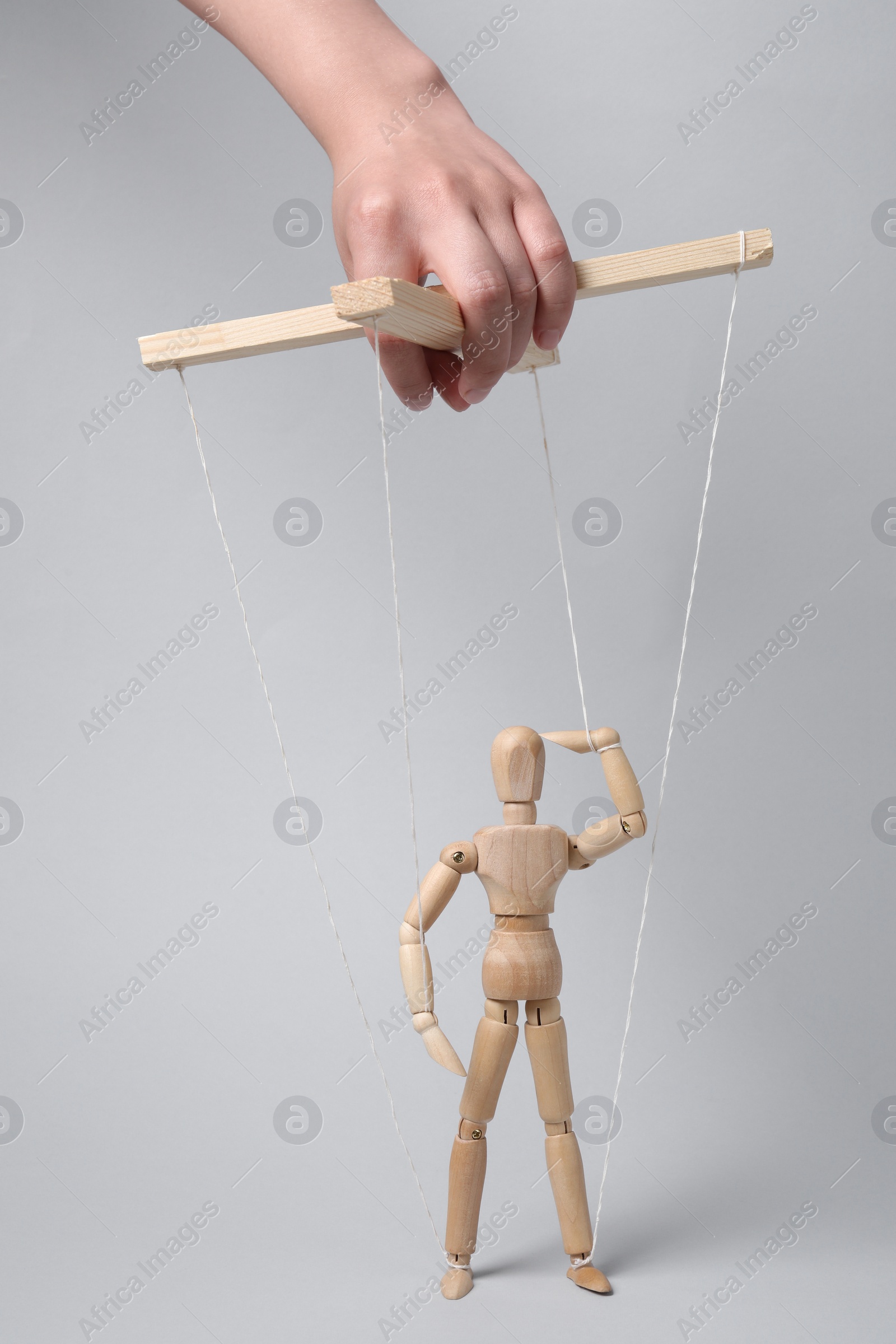 Photo of Woman pulling strings of puppet on light grey background, closeup