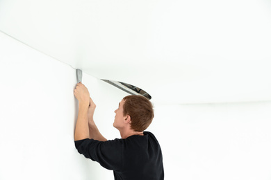 Photo of Repairman installing white stretch ceiling in room