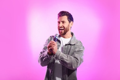 Photo of Handsome man with microphone singing on pink background