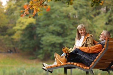 Photo of Affectionate senior couple with dry leaves spending time together in autumn park, space for text