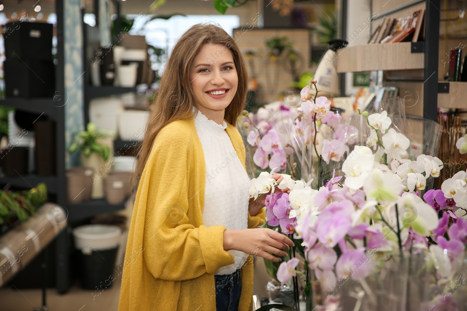 Photo of Beautiful young woman with orchids in flower shop