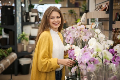 Photo of Beautiful young woman with orchids in flower shop