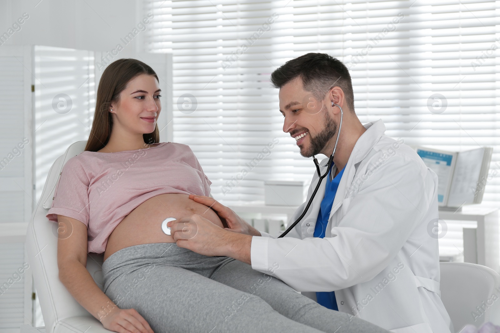 Photo of Doctor examining pregnant woman with stethoscope in clinic