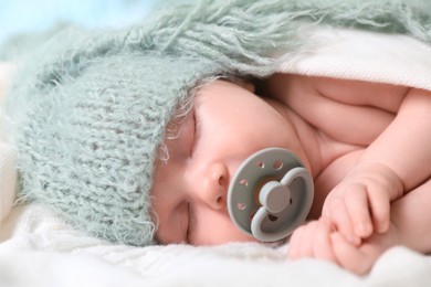 Photo of Cute newborn baby with pacifier sleeping on white blanket, closeup