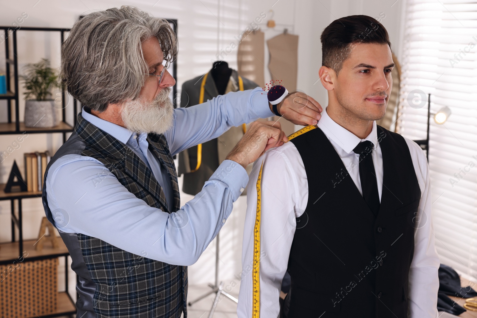 Photo of Professional tailor measuring shoulder seam length on client's vest in atelier
