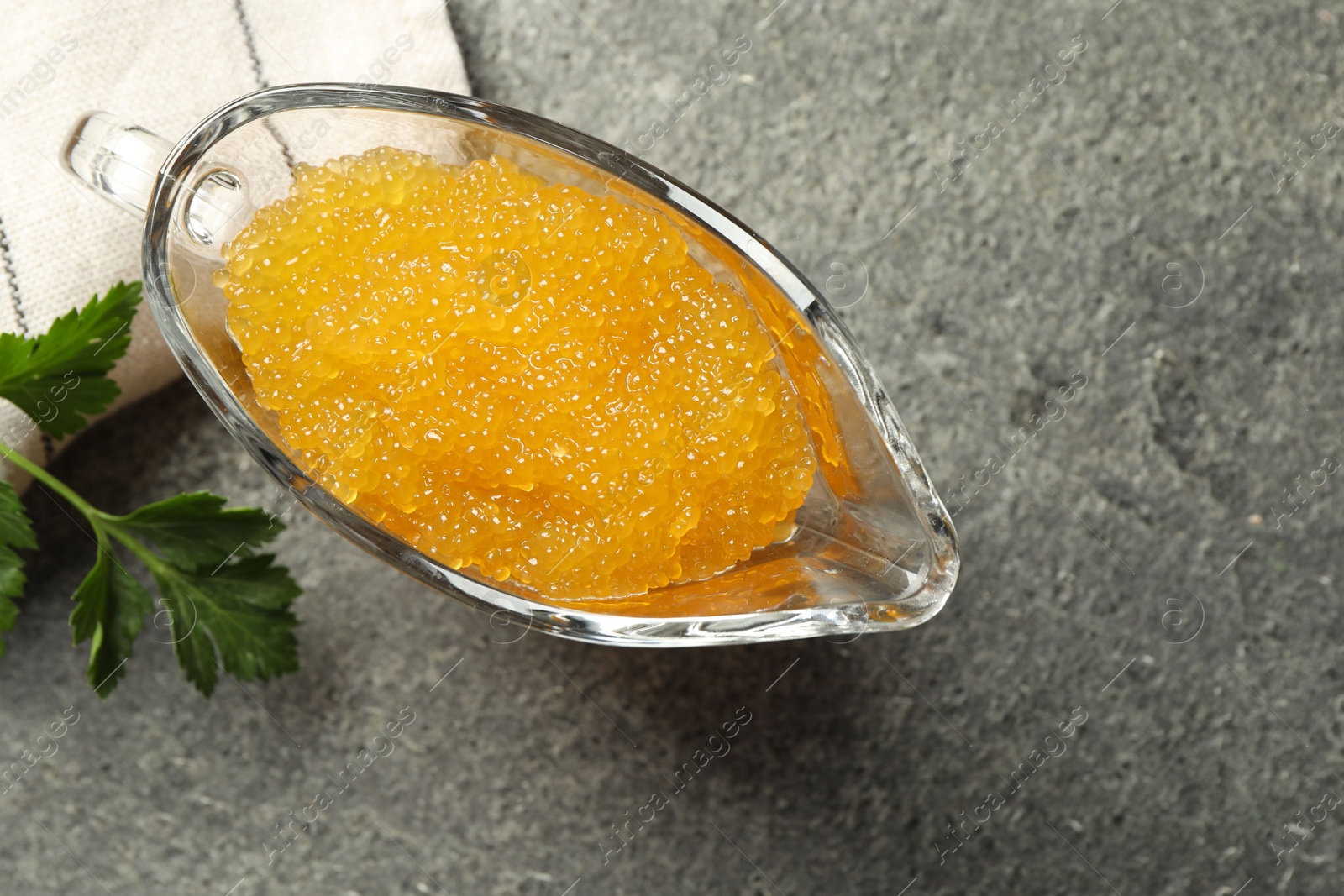 Photo of Fresh pike caviar in gravy boat and parsley on grey table, top view