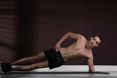 Photo of Handsome man doing side plank exercise on floor indoors