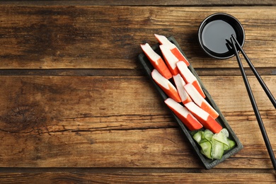 Photo of Fresh crab sticks with cucumber served on wooden table, flat lay. Space for text