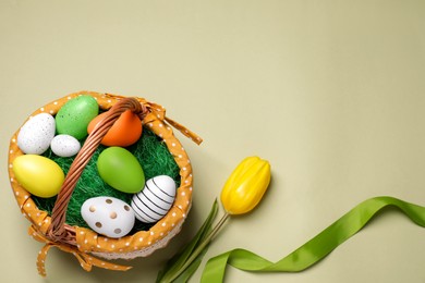 Easter basket with painted eggs, ribbon and tulip on color background, flat lay. Space for text
