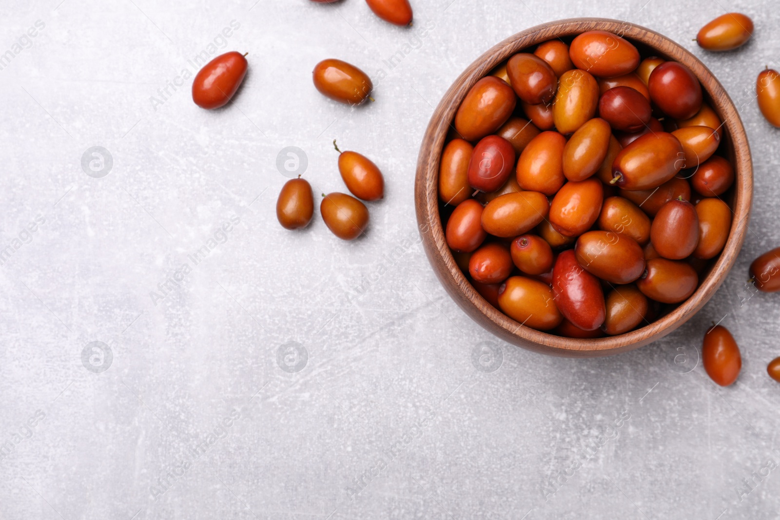 Photo of Fresh Ziziphus jujuba fruits with bowl on light table, flat lay. Space for text