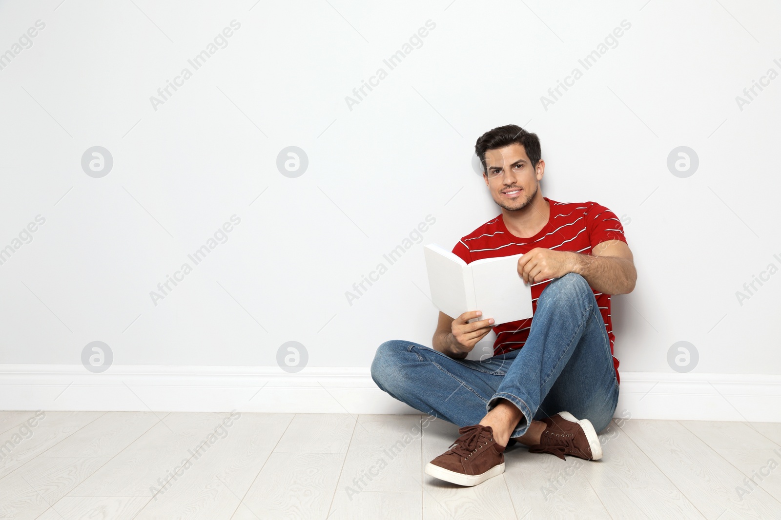 Photo of Handsome man reading book on floor near white wall, space for text