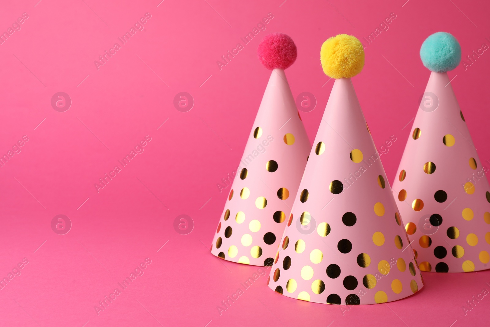 Photo of Beautiful party hats with pompoms on pink background, space for text