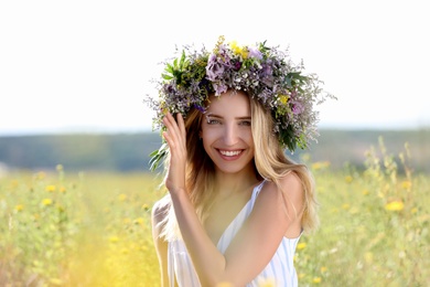 Young woman wearing wreath made of beautiful flowers in field on sunny day