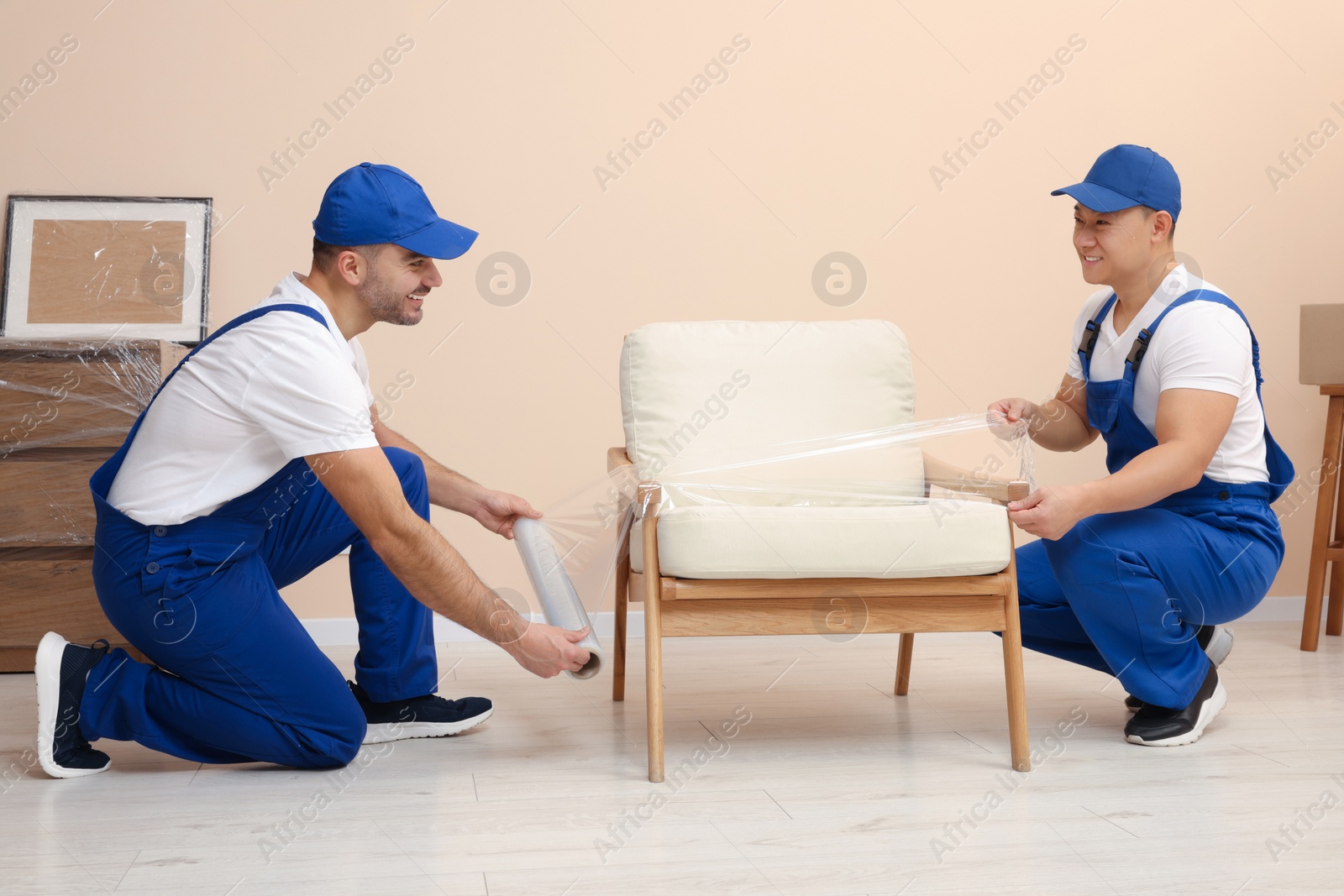 Photo of Workers wrapping armchair in stretch film indoors