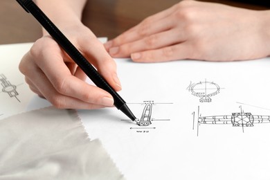 Jeweler drawing sketch of elegant ring on paper at table, closeup