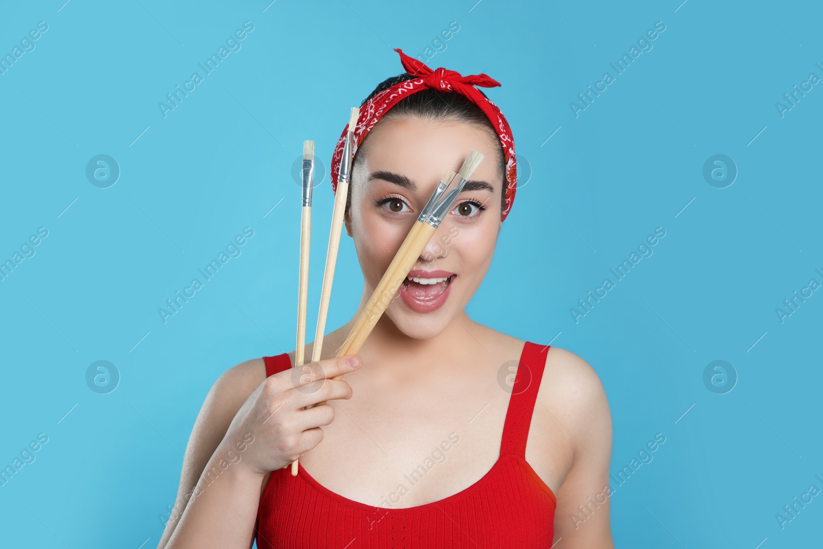 Photo of Woman with paintbrushes on light blue background. Young artist