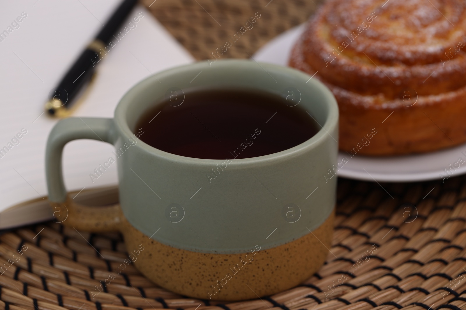 Photo of Cup of tea, pastry and notebook on wicker mat, closeup