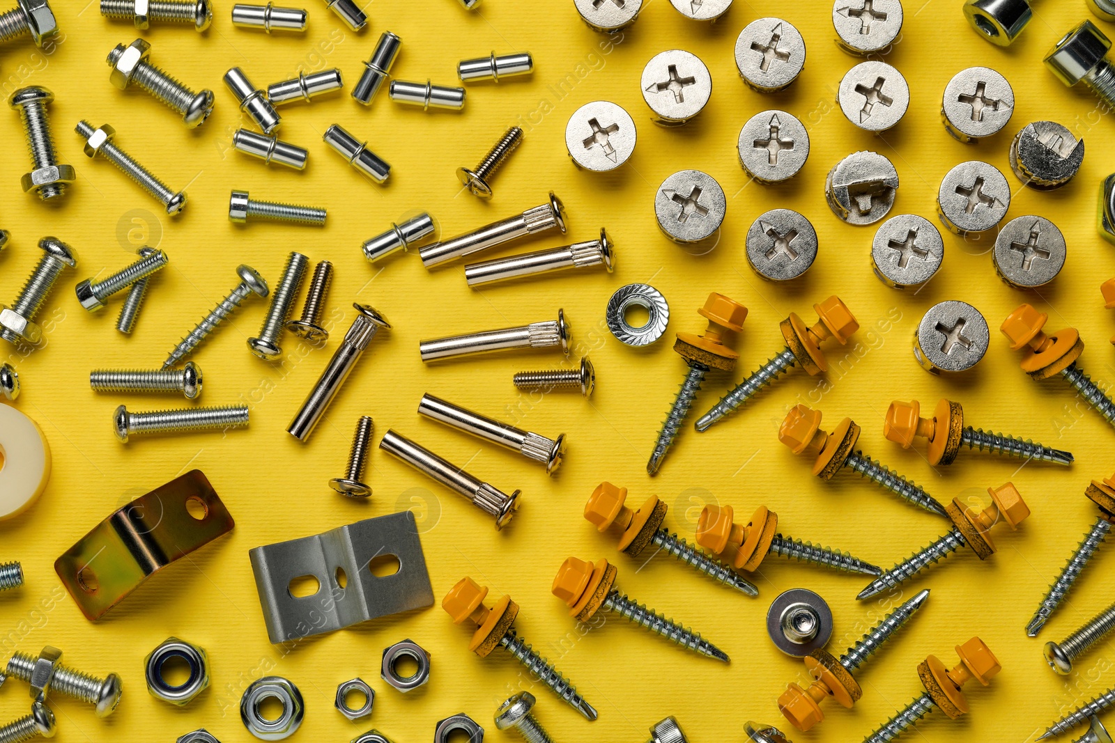 Photo of Many different fasteners on yellow background, flat lay