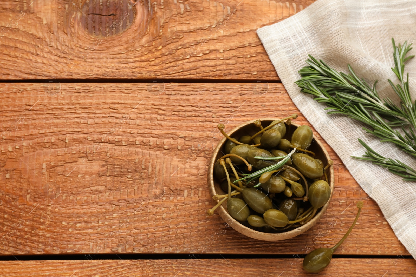 Photo of Delicious pickled capers and rosemary twigs on wooden table, flat lay. Space for text 