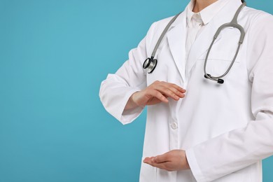 Doctor with stethoscope holding something on light blue background, closeup. Space for text