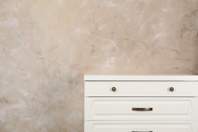 Photo of Modern chest of drawers near beige wall. Space for text