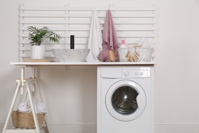 Photo of Laundry room interior with modern washing machine and stylish vessel sink on white wooden countertop