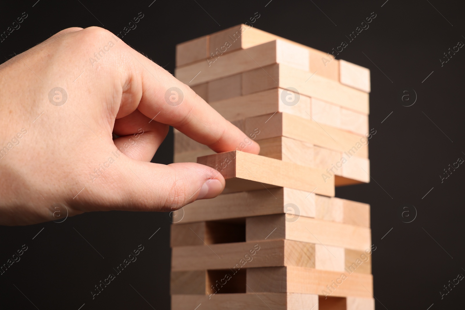 Photo of Playing Jenga. Man removing wooden block from tower on dark background, closeup